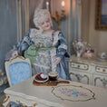 Load image into Gallery viewer, Porcelain doll in a vintage setting with a table and chair.

