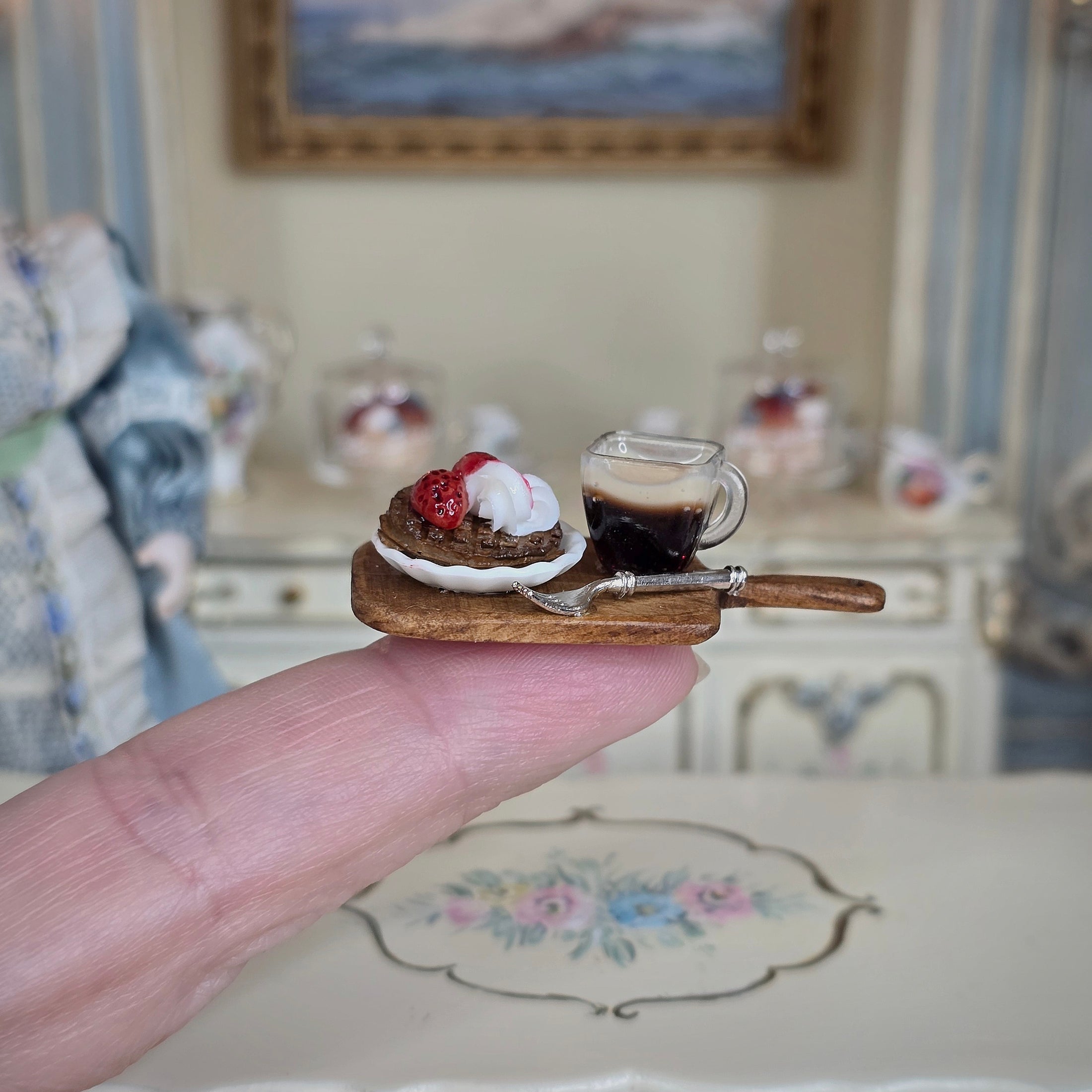 Miniature dessert with a glass of coffee on a cracker held between fingers, with a decorative background.