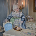 Load image into Gallery viewer, Vintage-style doll in a decorative setting with a table and chair.
