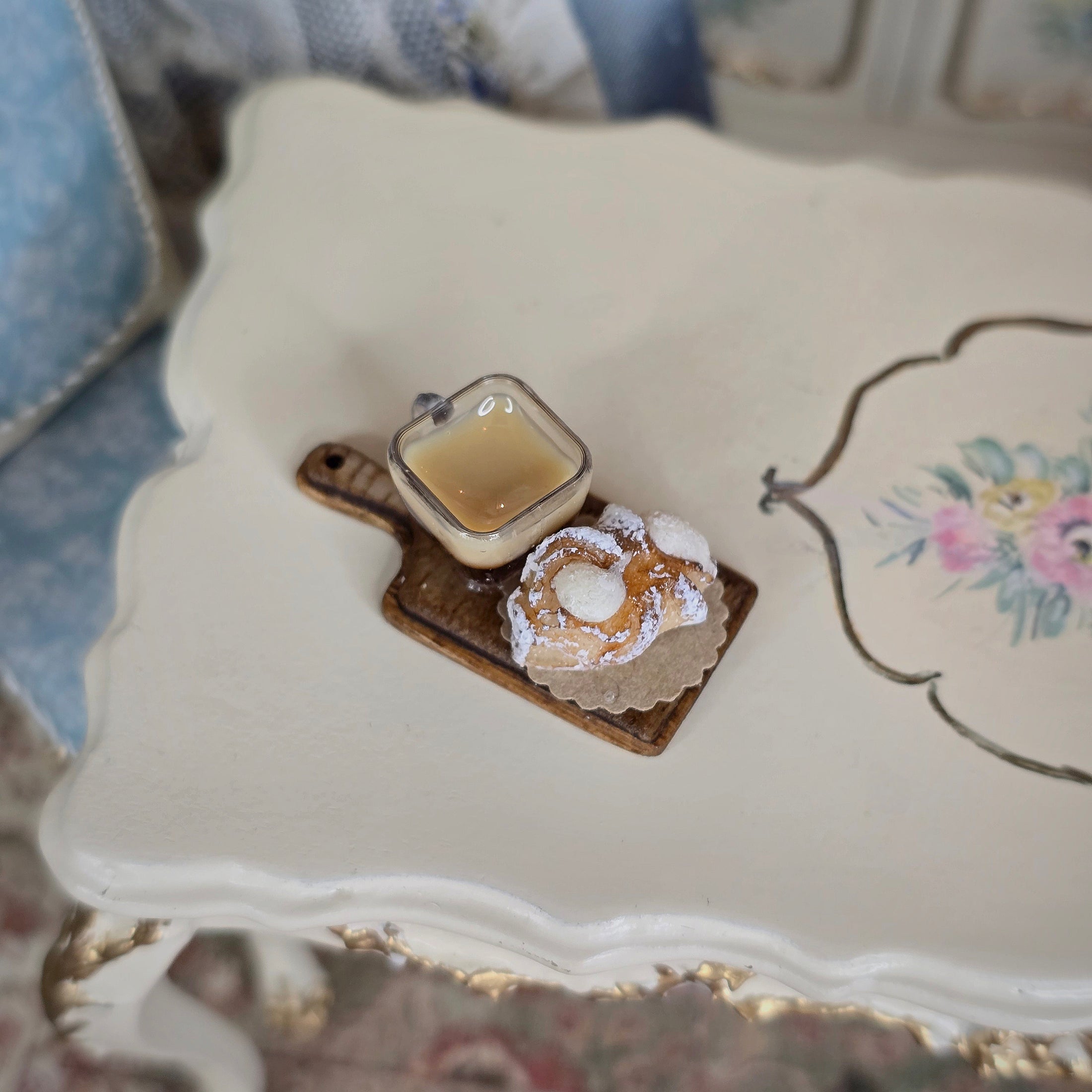 Miniature scene of a coffee cup and cake on a decorative plate with floral design.