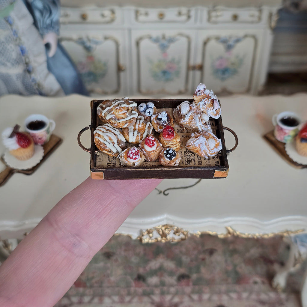 Miniature tray with pastries held by a finger in front of a decorative background