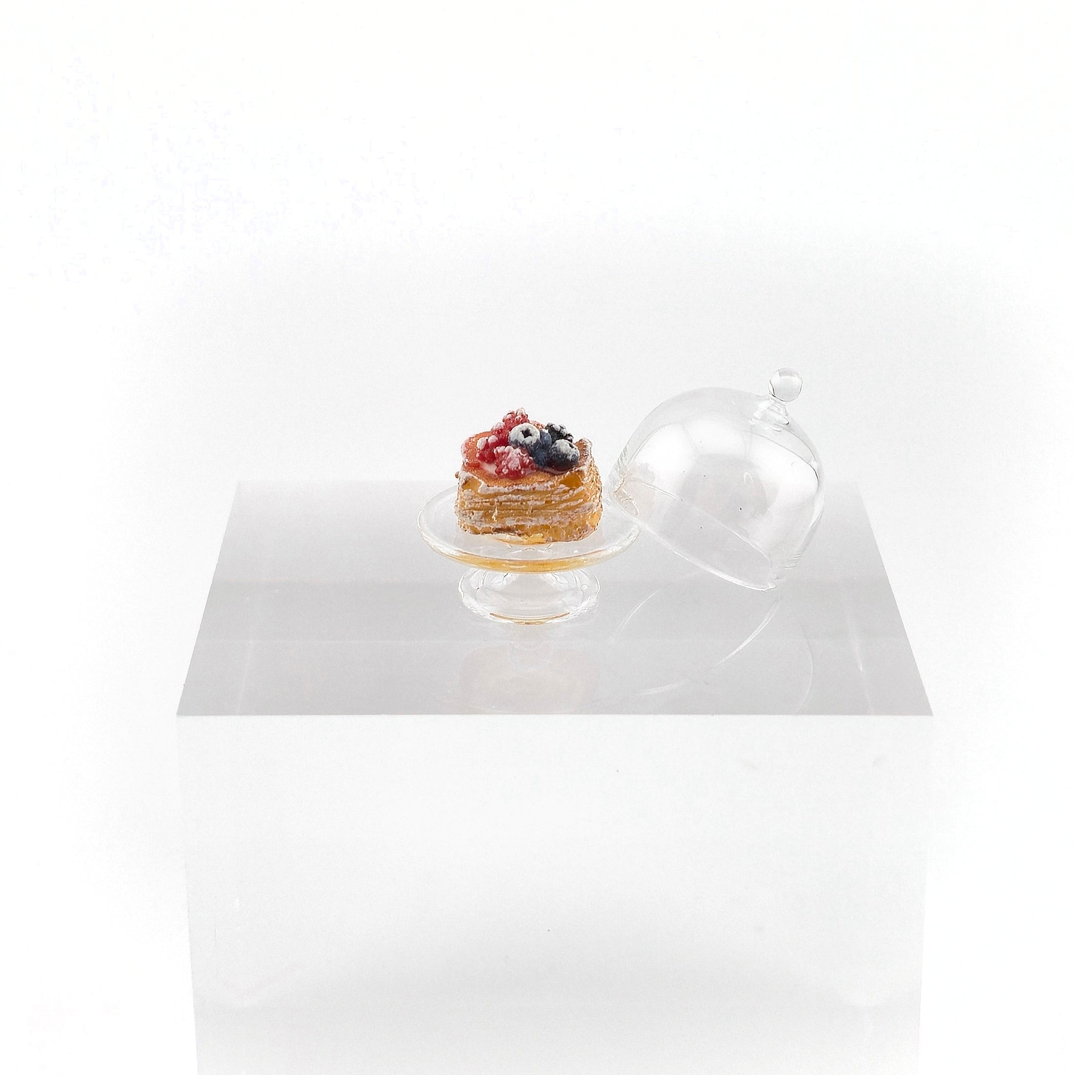 Small pastry on a stand with a clear dome cover on a white background