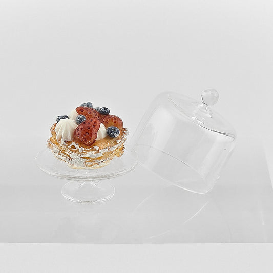 Small dessert on a white stand with a clear lid on a white background
