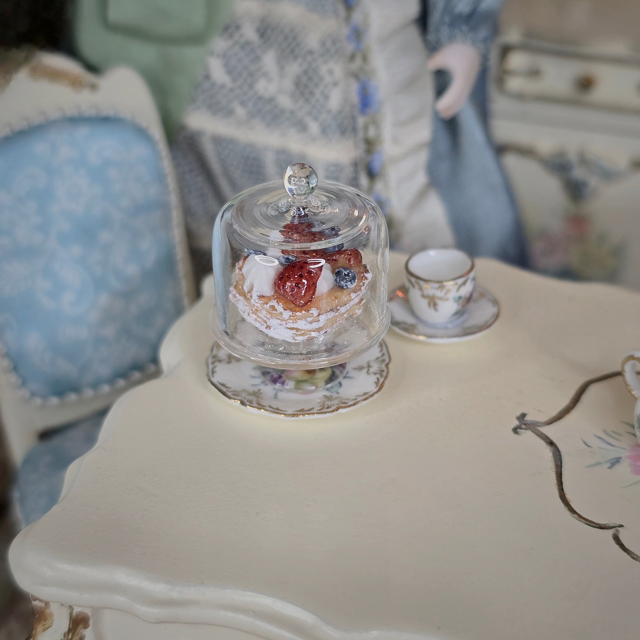 Small pastry/tart under a clear dome on a table with a blurred background