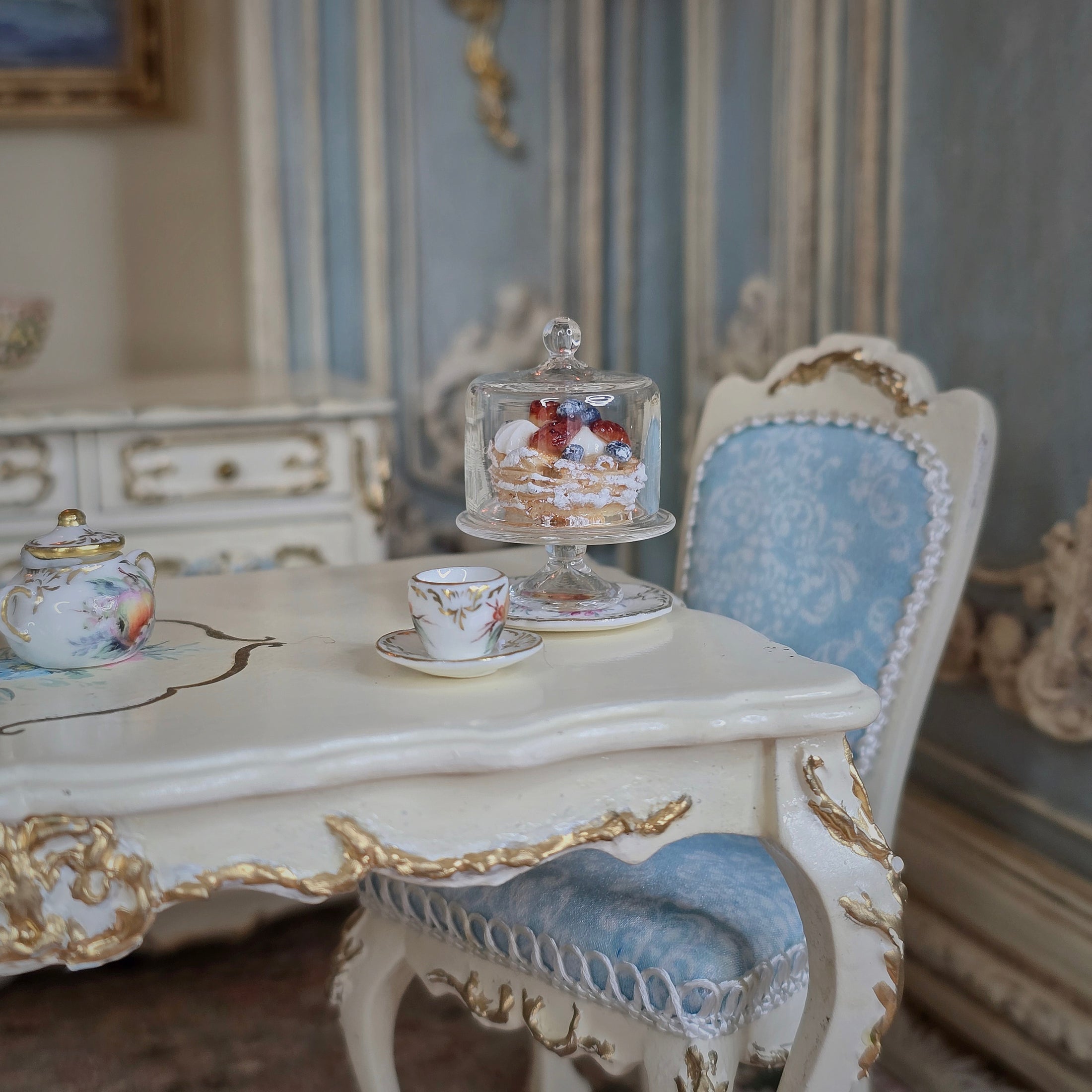 Miniature tea set and pastry on a decorative table with ornate chair in a detailed room setting
