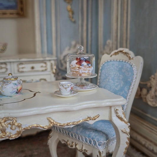 Miniature tea set and pastry on a decorative table with ornate chair in a detailed room setting