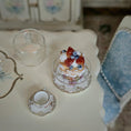 Load image into Gallery viewer, Miniature cake and teacup set on a decorative table with floral patterns.
