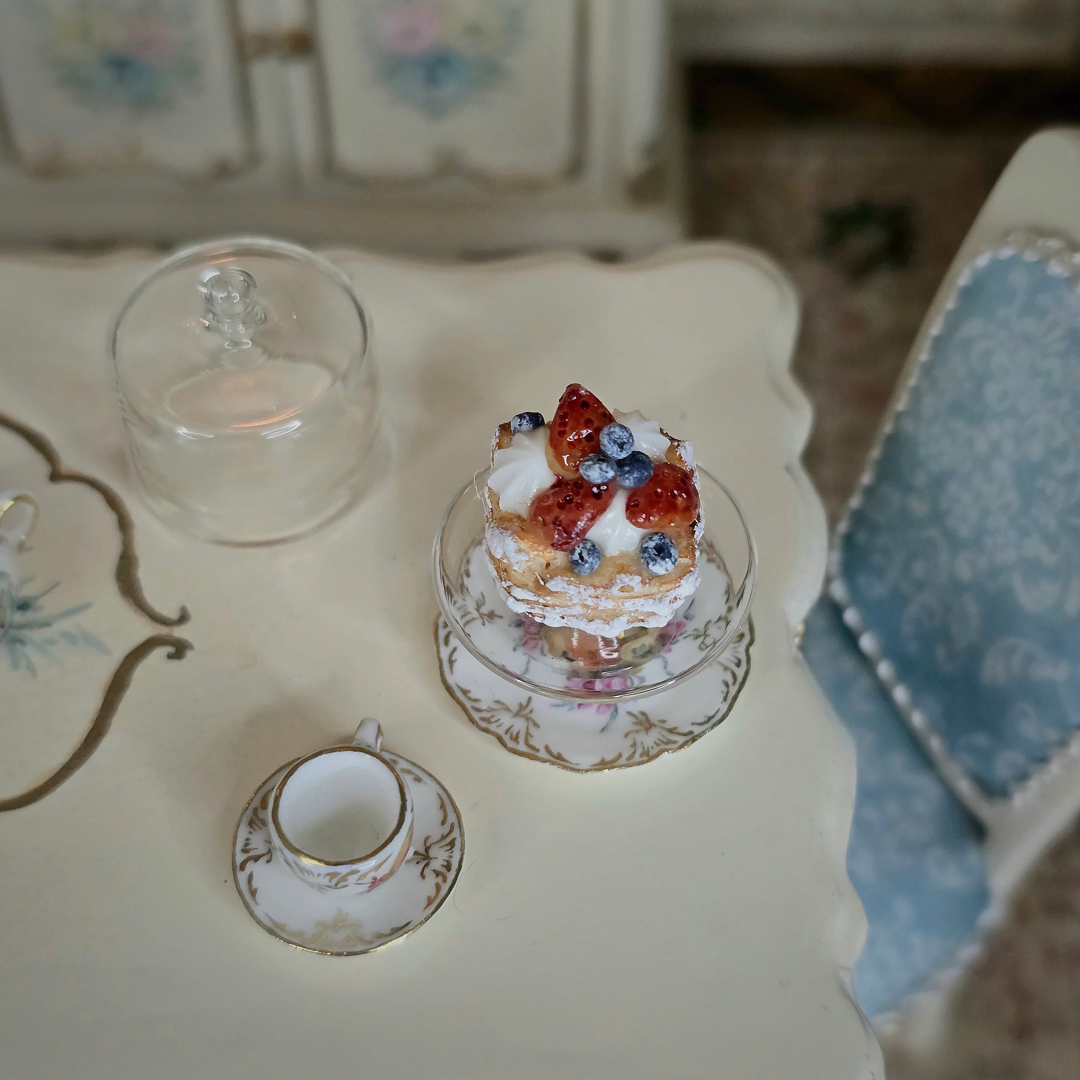 Miniature cake and teacup set on a decorative table with floral patterns.