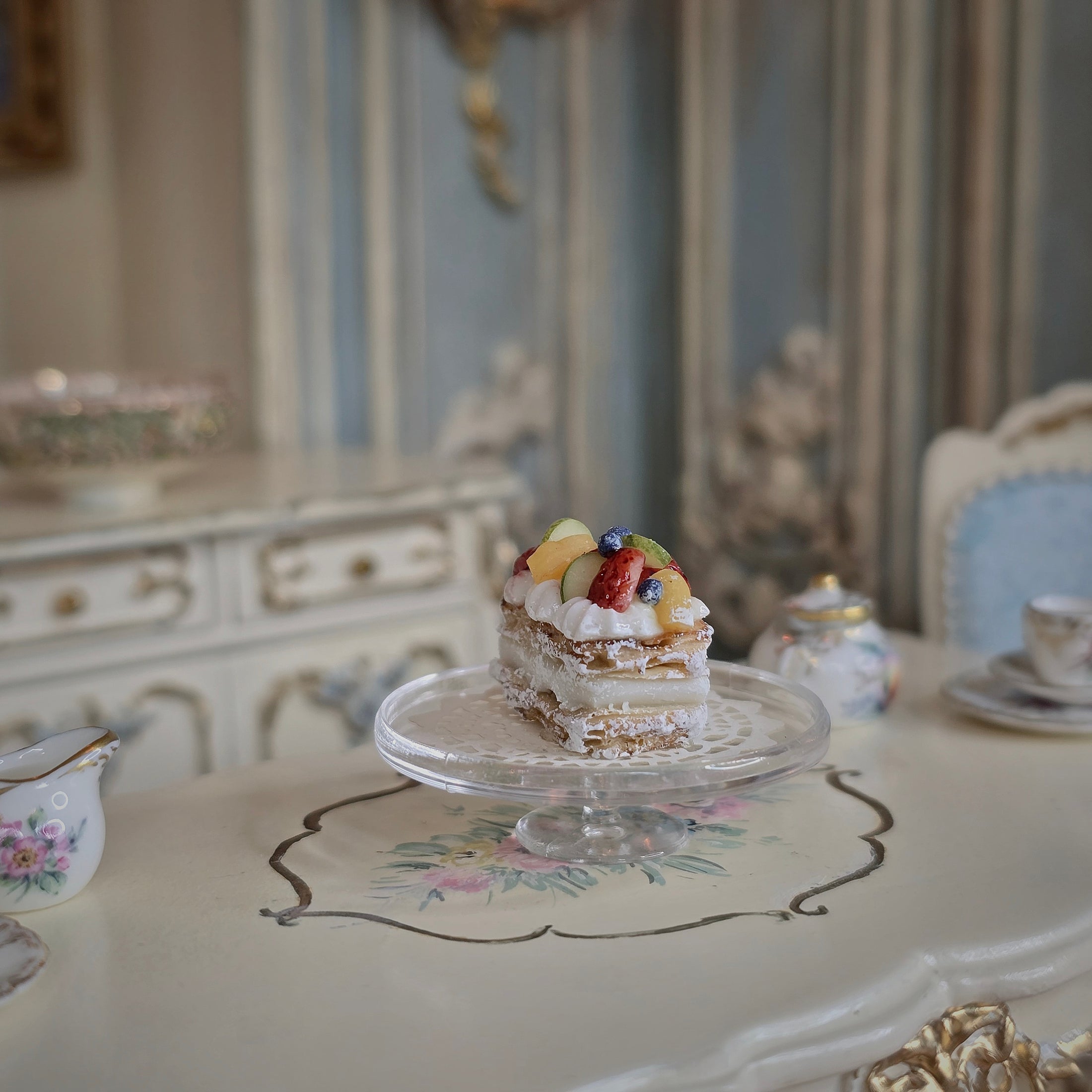 Long fruit tart on a glass plate with a decorative tablecloth and vintage furniture in the background