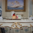 Load image into Gallery viewer, Decorative cupcake and mug on a ornate surface with a blurred painting in the background
