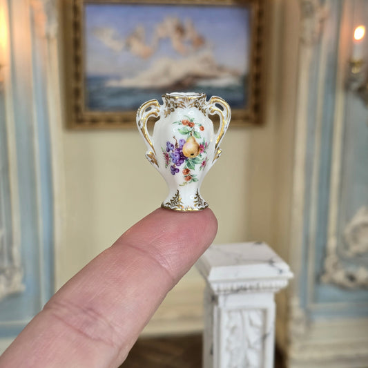 Miniature ornate vase held on a single finger with a decorative interior background