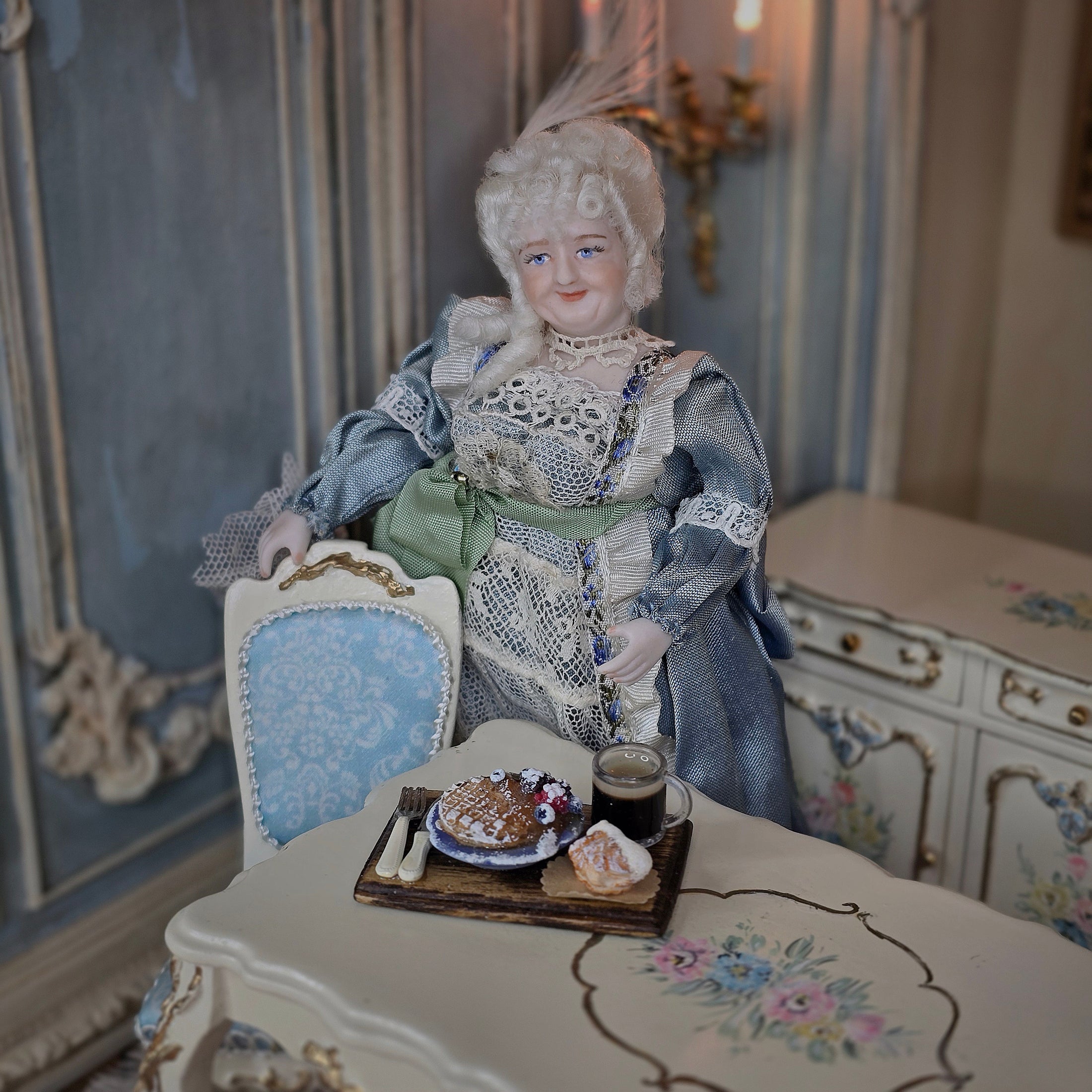 Vintage-style doll in a decorative setting with a table and chair.