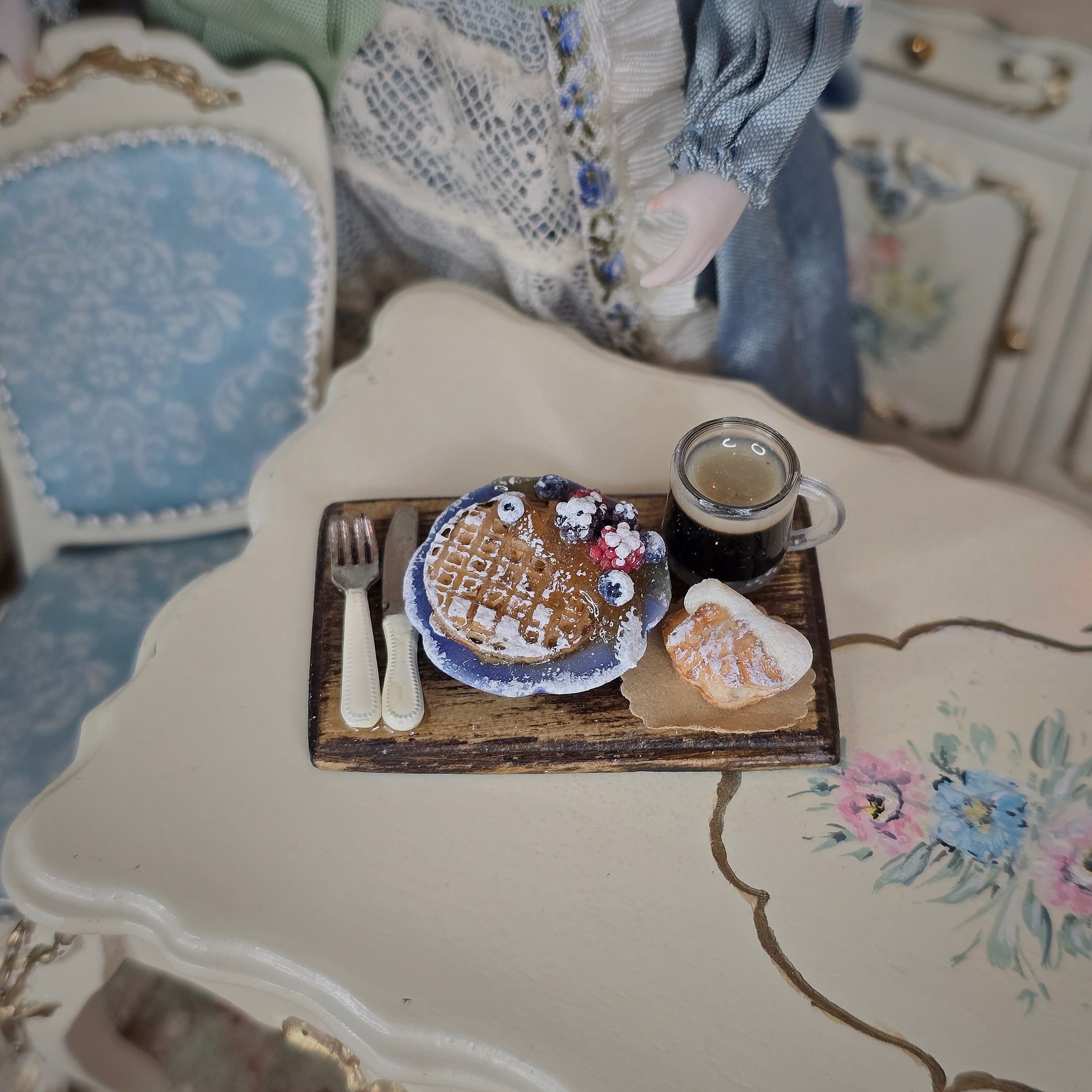 Miniature waffle with decorative plate and coffee cup on a floral table.