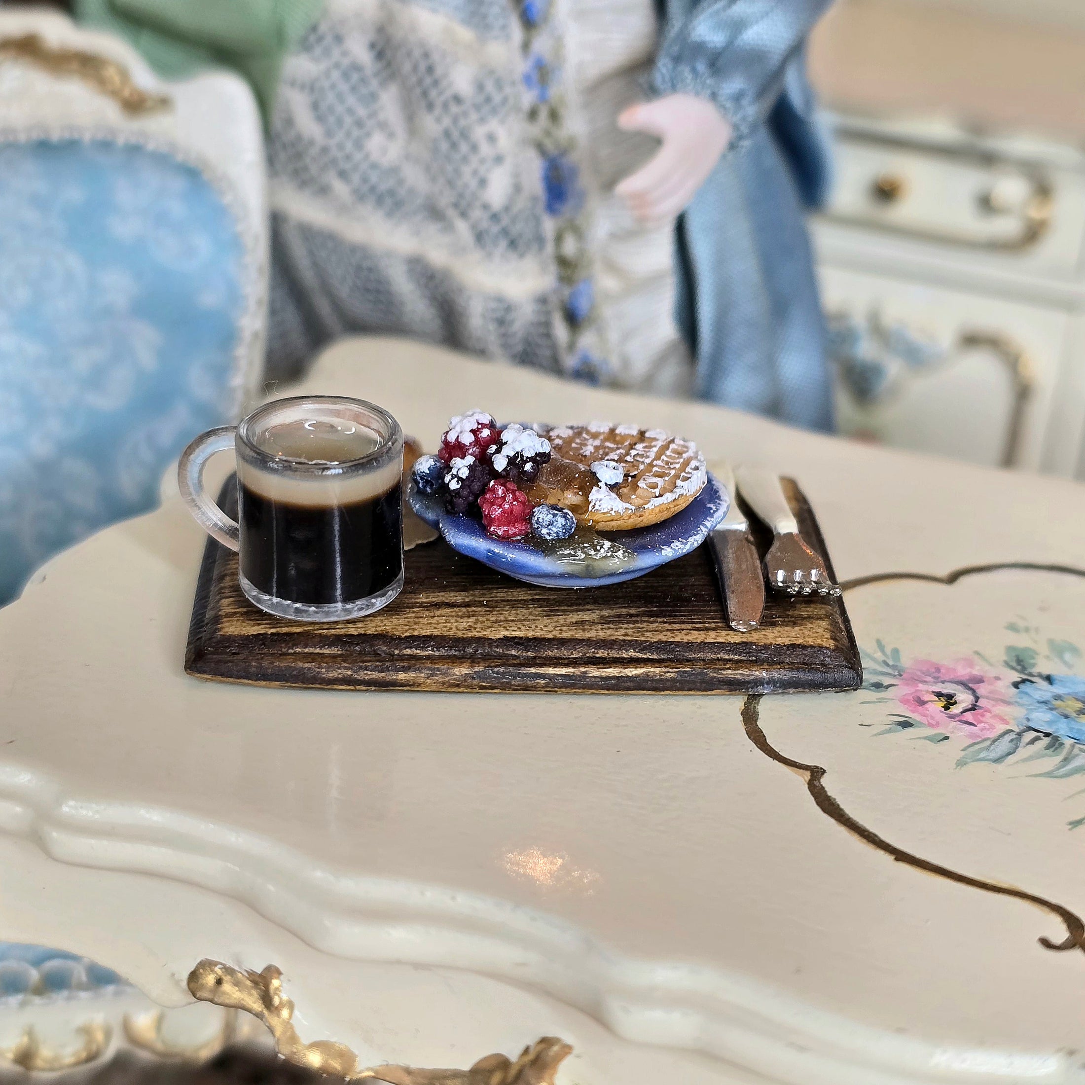 Miniature waffle with berries and a glass of coffee on a wooden tray in a decorative setting.