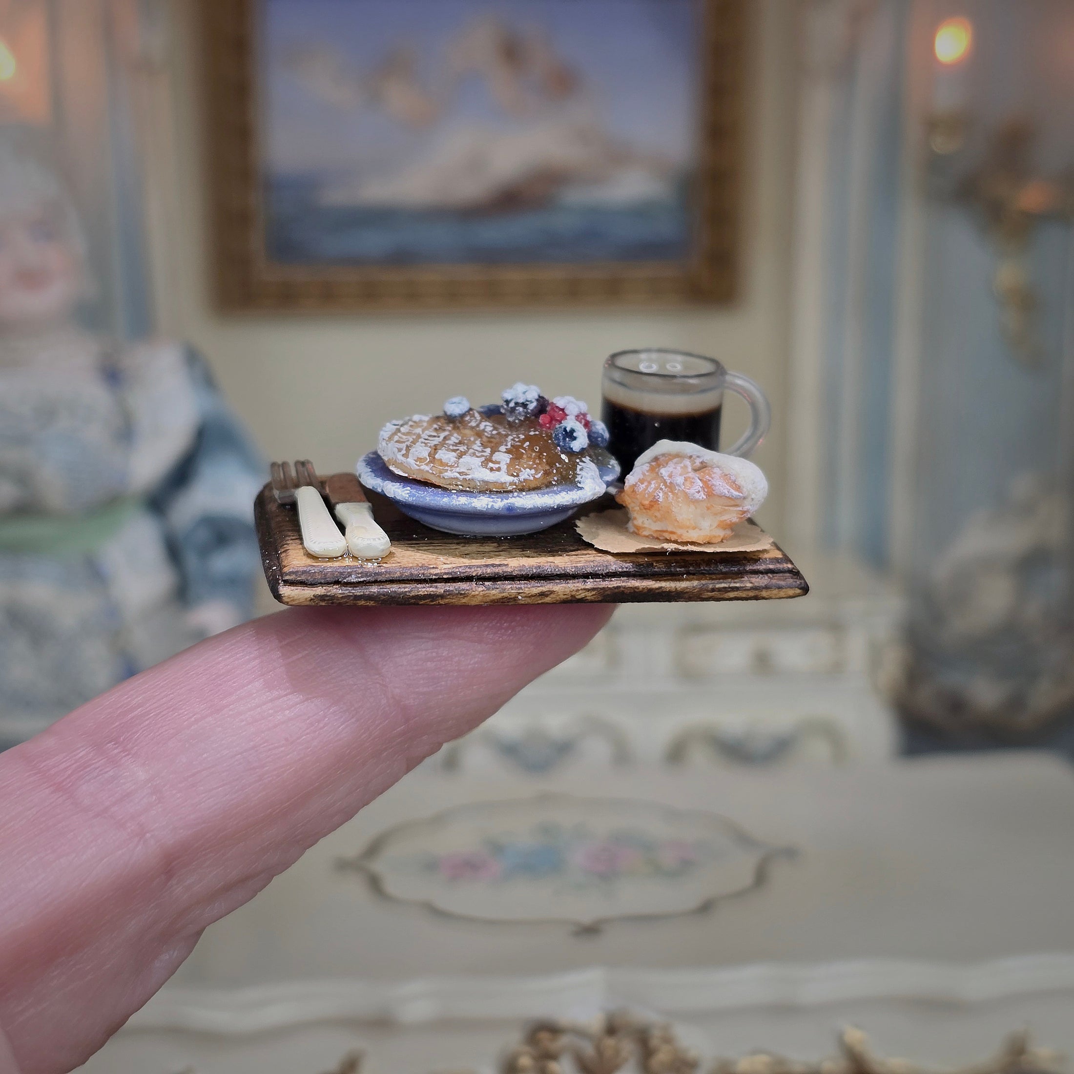 Miniature food and drink set on a wooden tray held by a hand, with a blurred background