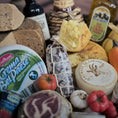 Load image into Gallery viewer, Assorted cheeses, meats, and condiments on a wooden board with a blurred background.
