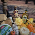 Load image into Gallery viewer, Assorted food items including bottles, bread, cheese, and vegetables on a rustic surface.

