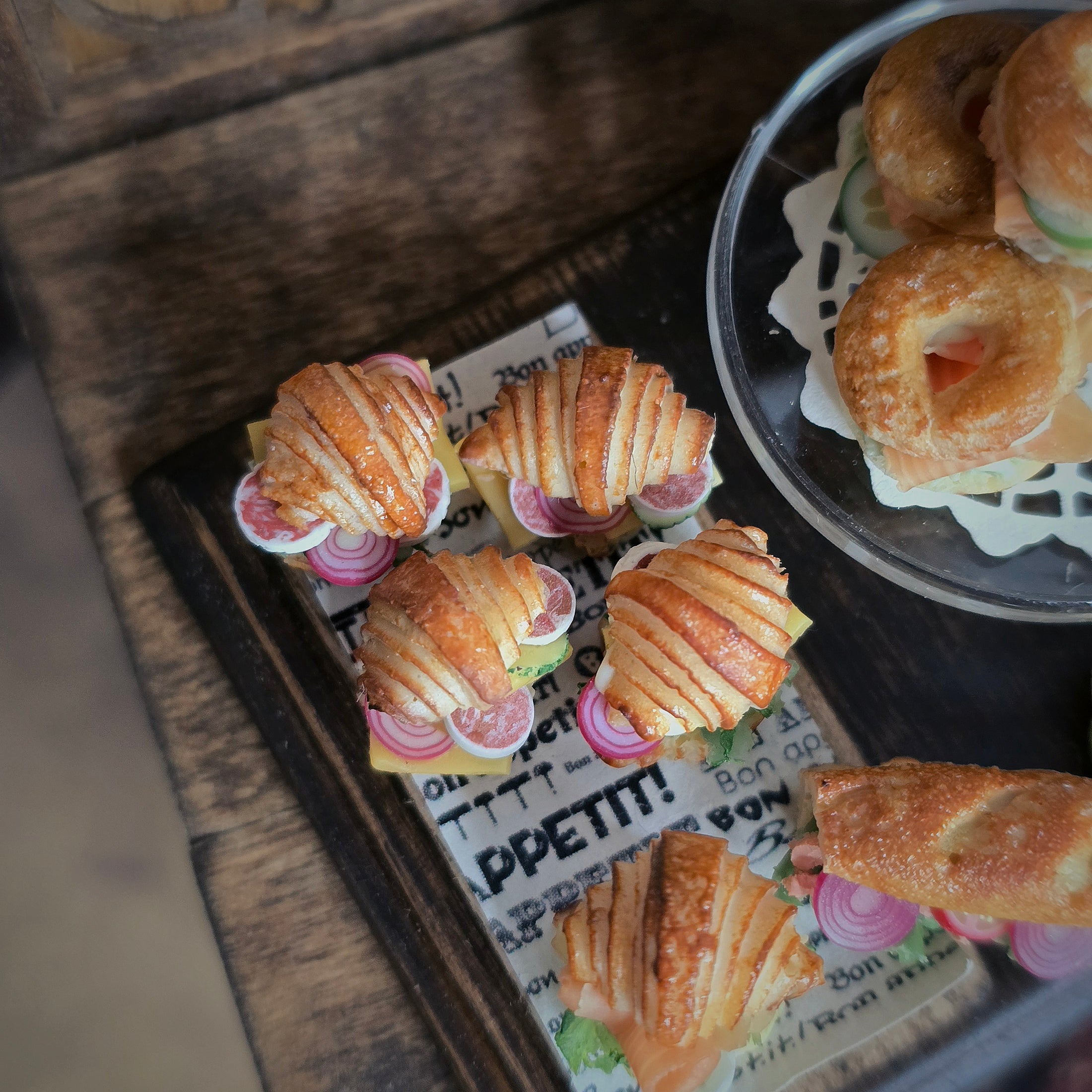 Small sandwiches on a tray with a newspaper underneath, on a wooden surface.