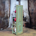 Load image into Gallery viewer, Small green door with decorative items on a textured surface
