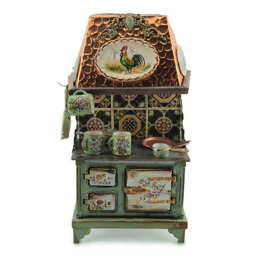 Decorative miniature stove with rooster design on the lid, surrounded by mugs and a teapot.
