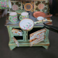 Load image into Gallery viewer, Miniature pan with floral design held by tweezers against a blurred miniature kitchen background.
