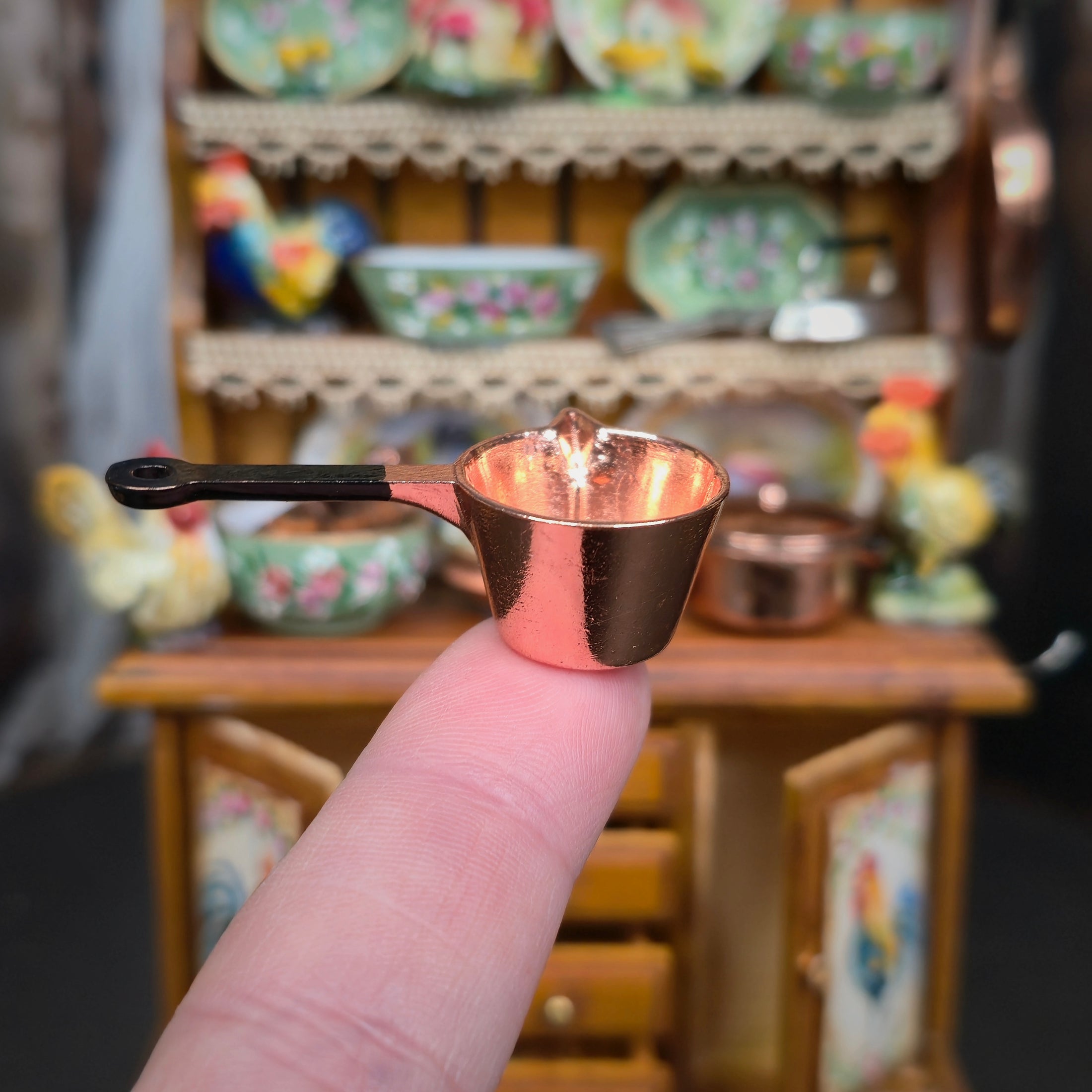 Small bronze pot held by a finger with a blurred background of ceramic dishes.