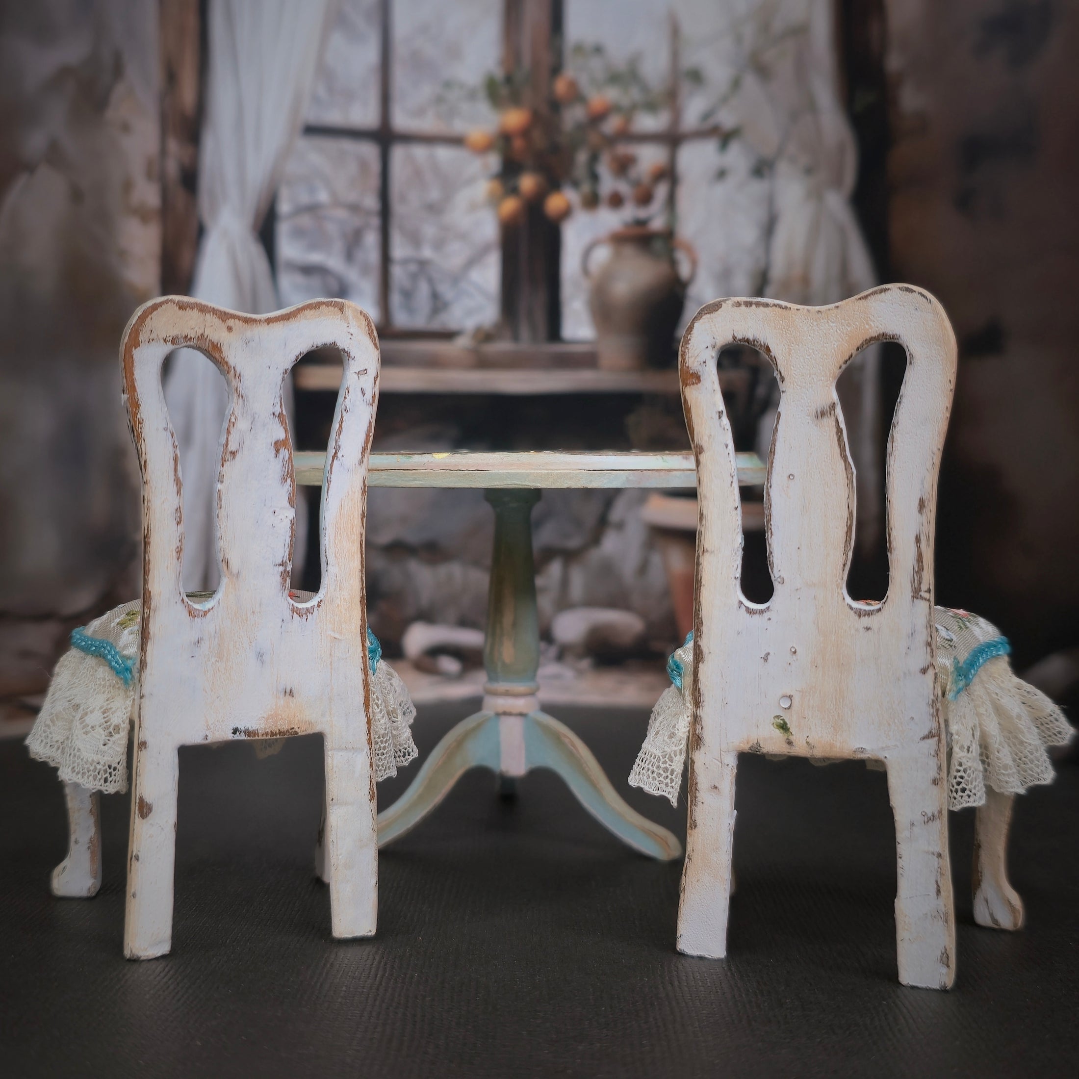 Two distressed white chairs with lace covers in front of a small table in a blurred indoor setting.