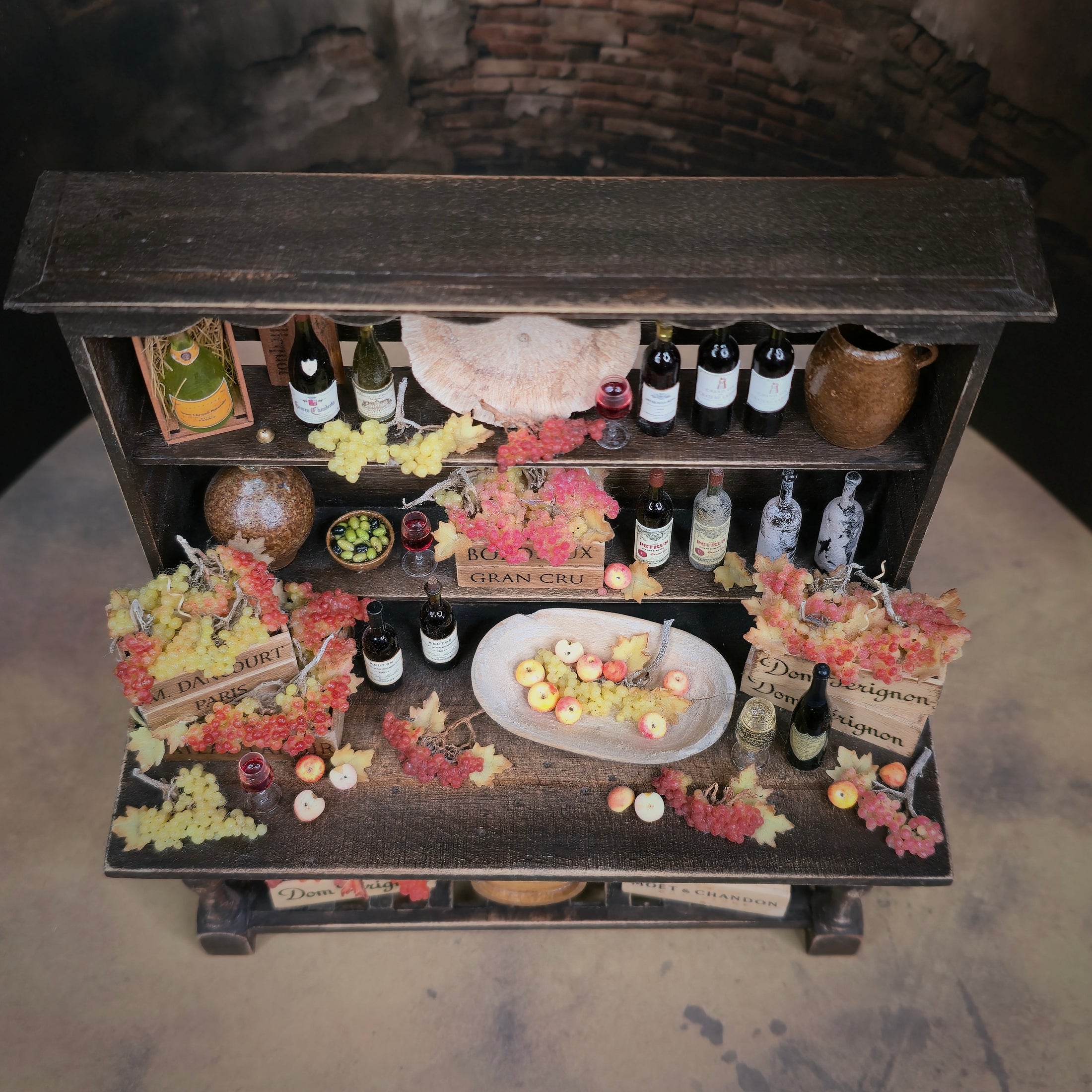 Miniature bar setup with bottles, glasses, and decorative elements on a wooden shelf.