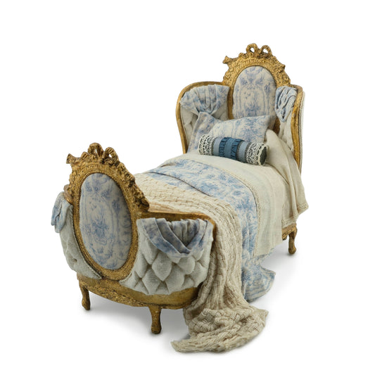 Decorative bed with gold frame and blue and white patterned coverings on a white background
