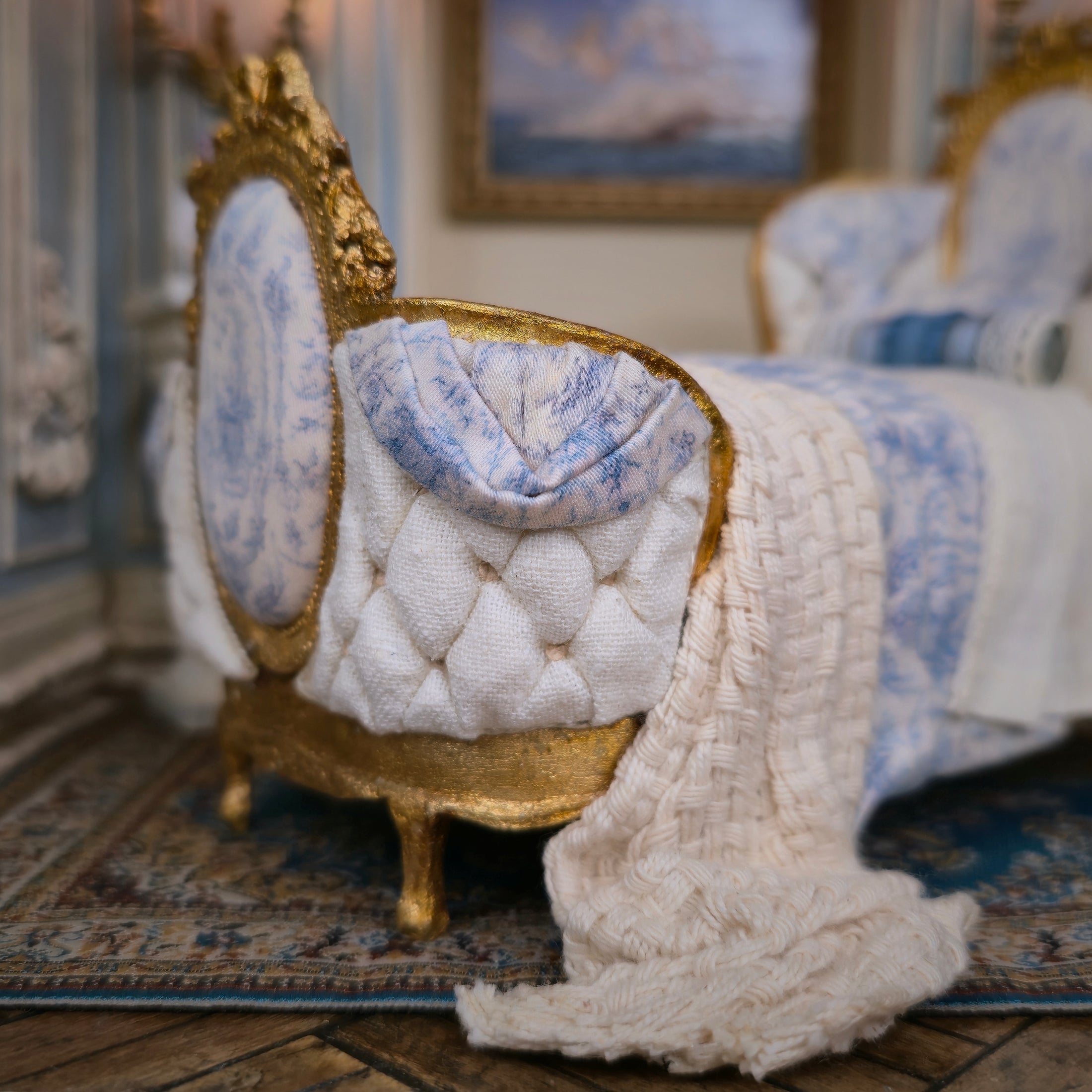 Close-up of a decorative bed with gold frame and white quilt in a room setting.
