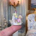 Load image into Gallery viewer, Small figurine of two people held on a finger, with a decorative interior background.
