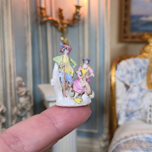 Small figurine of two people held on a finger, with a decorative interior background.