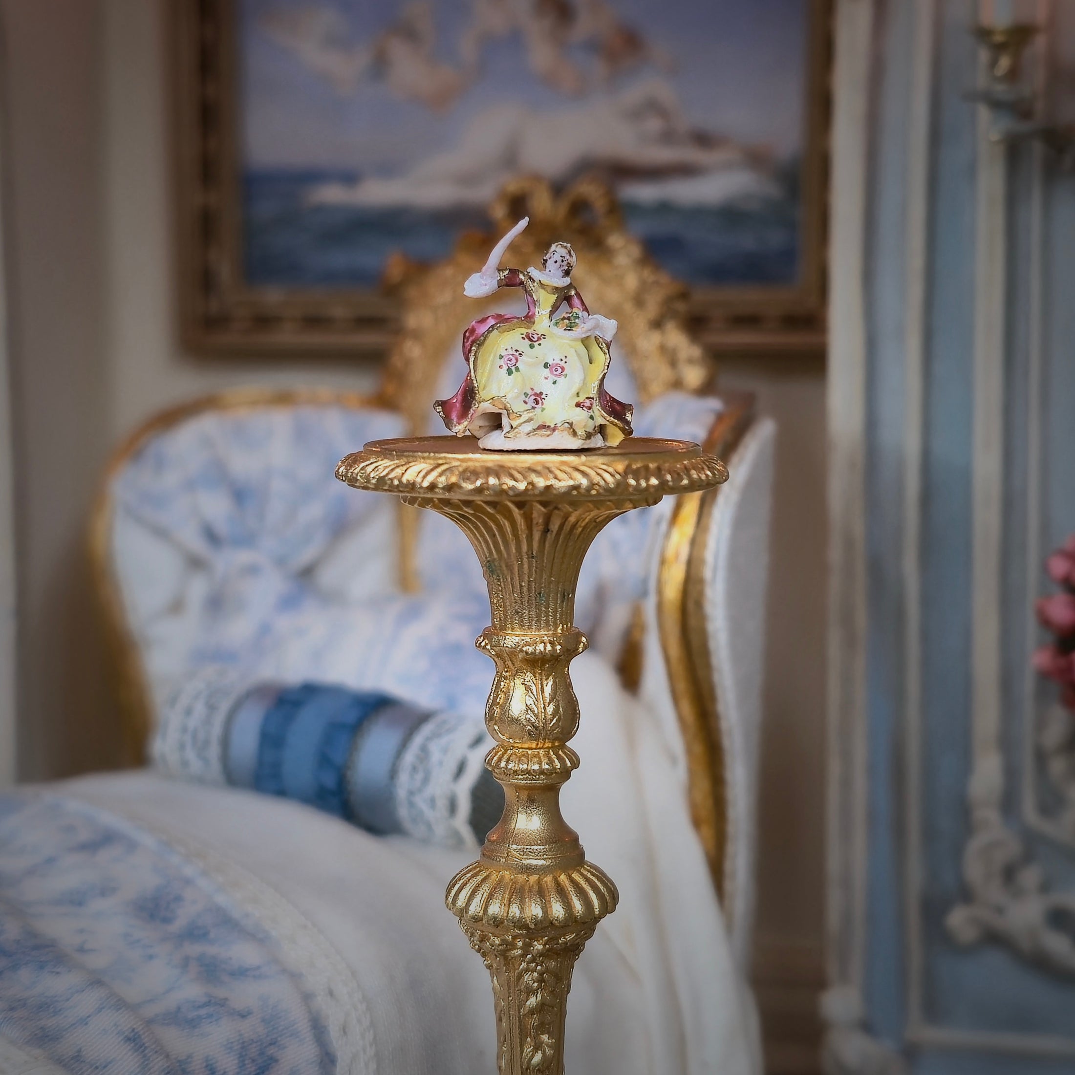 Decorative figurine on a gold pedestal in a room with a painting in the background