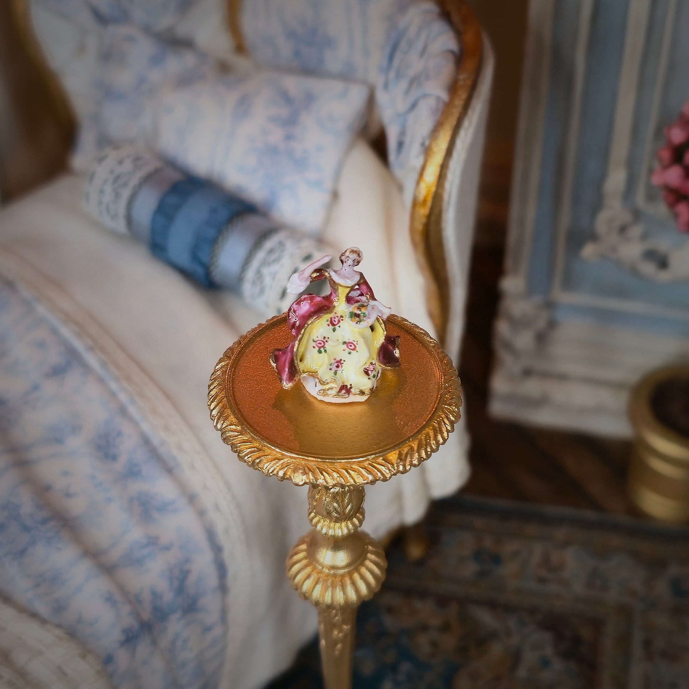Decorative figurine on a small gold pedestal in an elegant room setting.