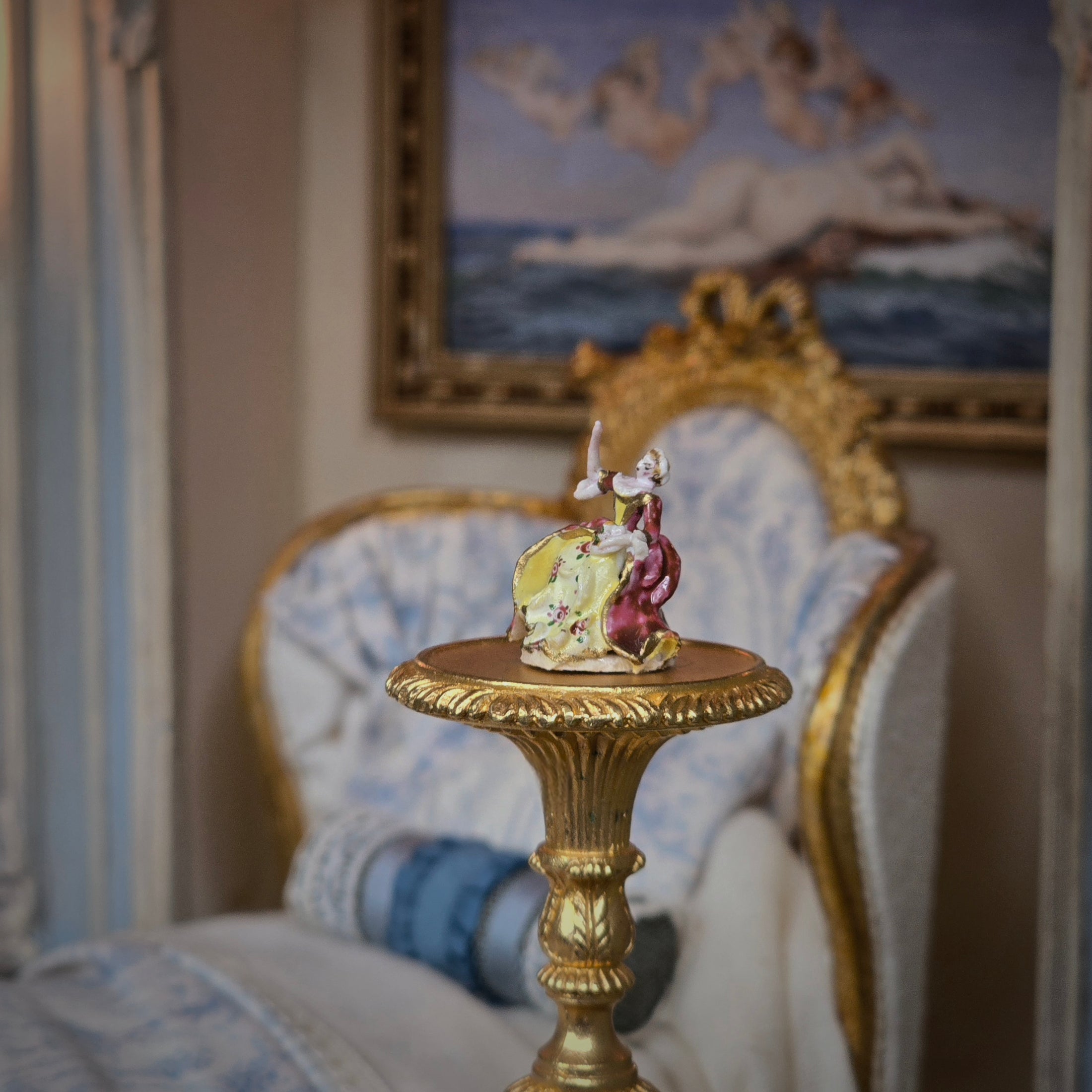 Decorative figurine on a gold pedestal in an elegant room with a painting in the background.