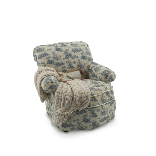 Floral patterned armchair with a blanket draped over it on a white background