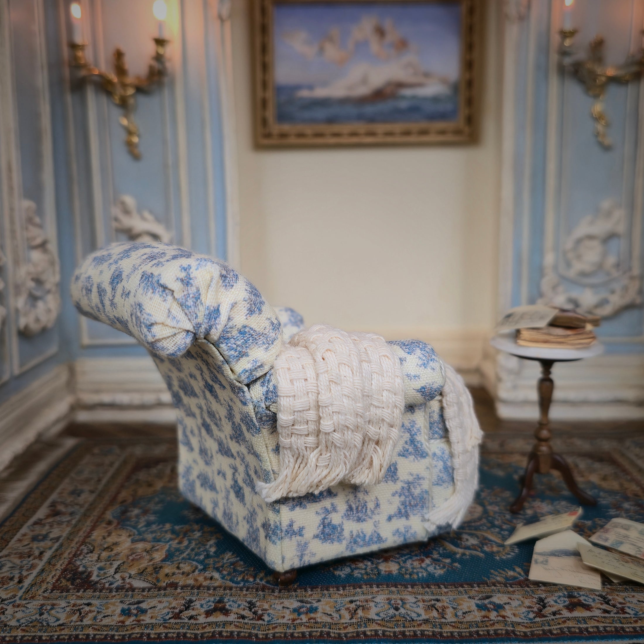 Decorative armchair with blue toile pattern in a room with striped walls and a small table.
