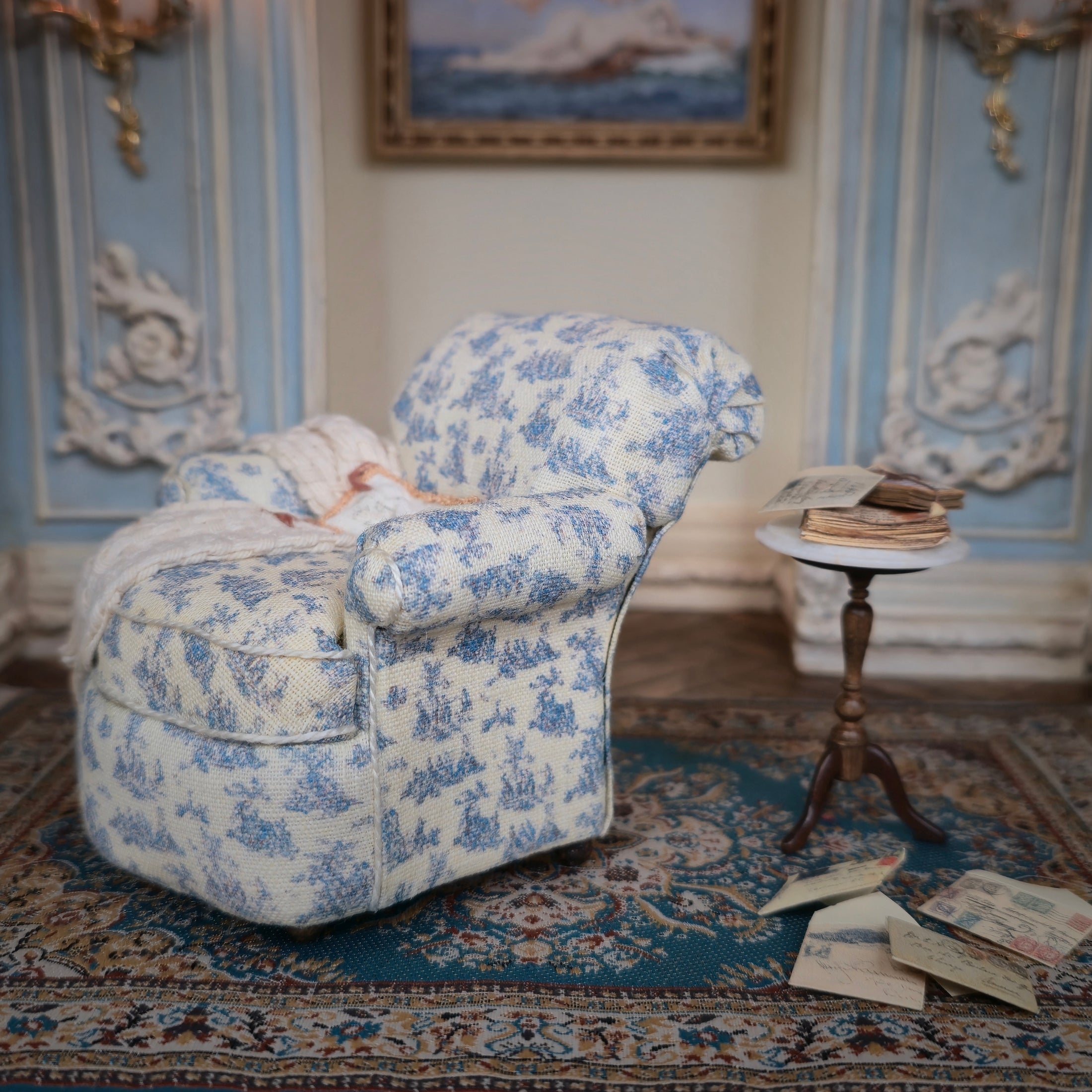 Decorative armchair with blue floral pattern in a room with ornate decor and books on a table.