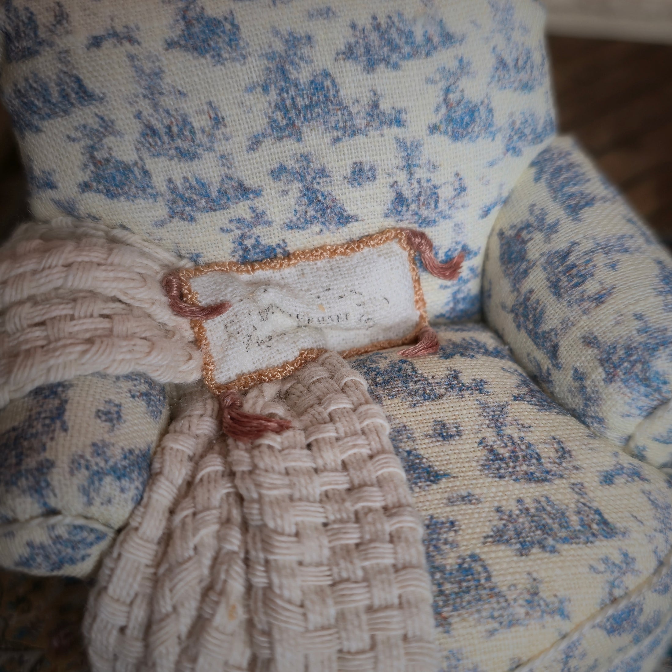 Close-up of a decorative pillow with blue floral pattern and braided trim on a chair.
