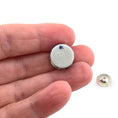 Load image into Gallery viewer, Small round white object with blue design held between fingers on a white background
