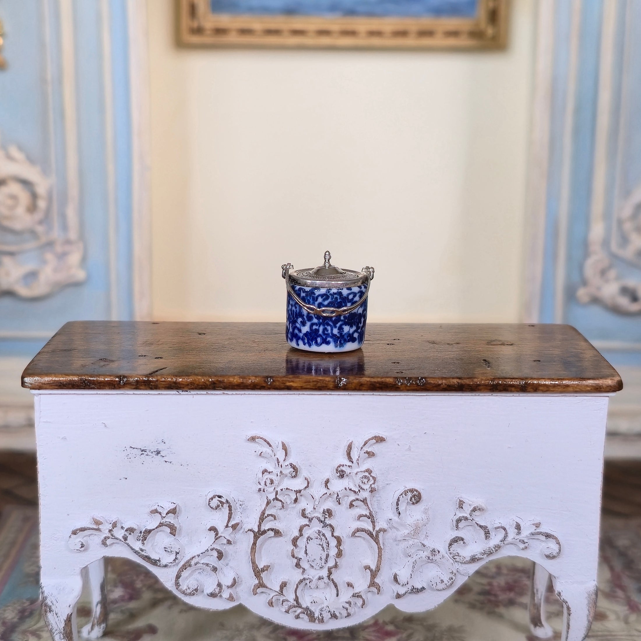 Decorative white chest with intricate carvings on a patterned rug, with a blue and white ceramic item on top.