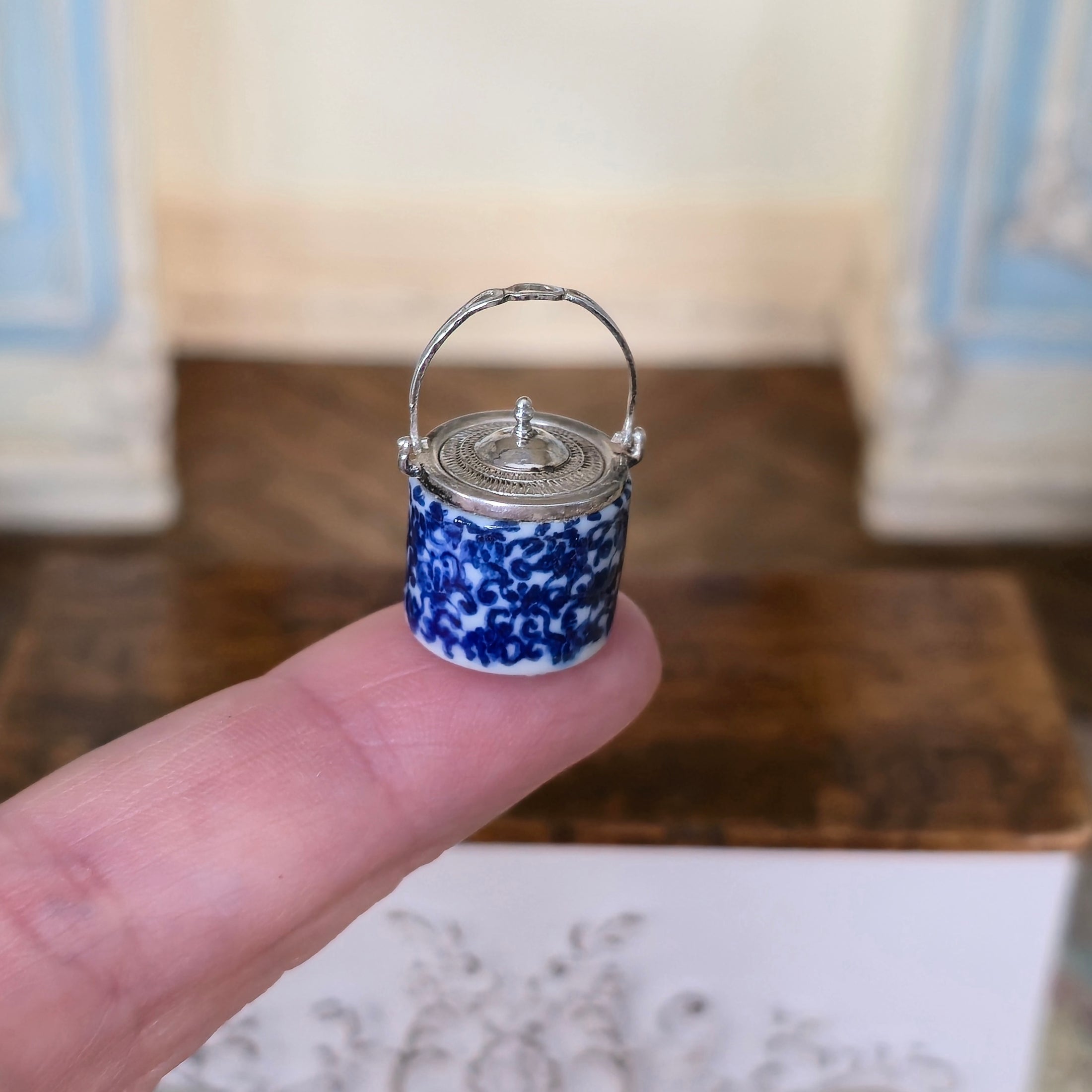 Miniature blue and white ceramic jar held between fingers with a blurred background