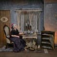 Load image into Gallery viewer, A gypsy woman doll sits in an old chair at a small table in a spooky, cobweb-filled room. She wears a black blouse with a purple floral skirt and a red-and-white head covering.
