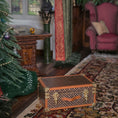 Load image into Gallery viewer, Decorative trunk on a patterned rug with a Christmas tree and chair in the background
