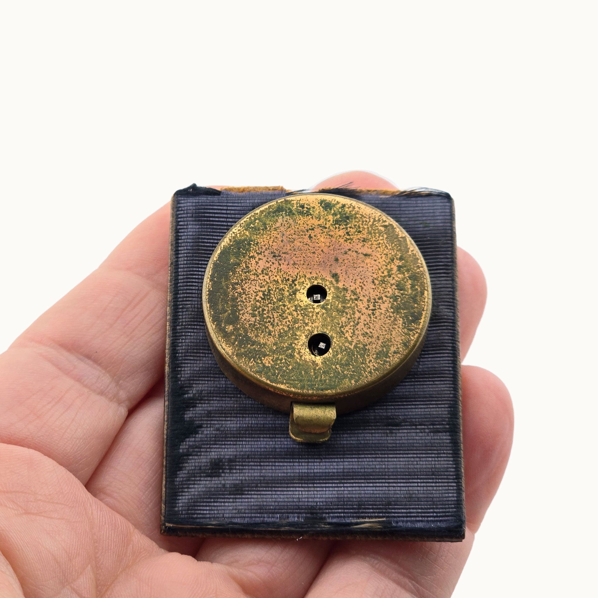 backside of piece showing antique brass clock held in a hand against a white background
