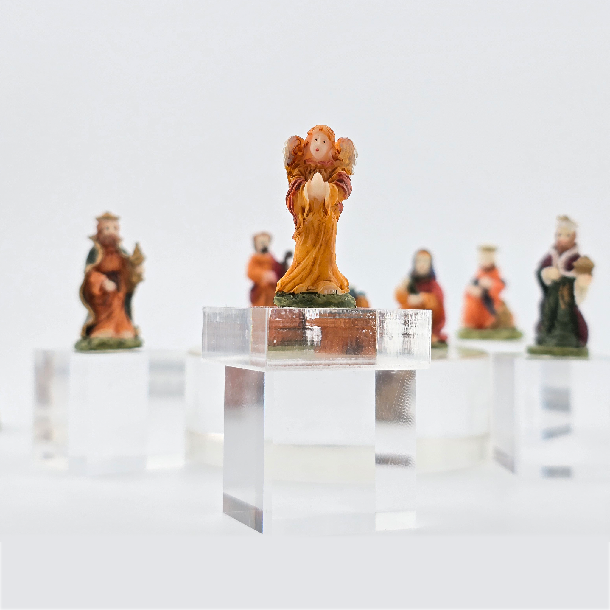 Decorative nativity angel miniature dollhouse figurine on a clear stand with other figurines in the background.