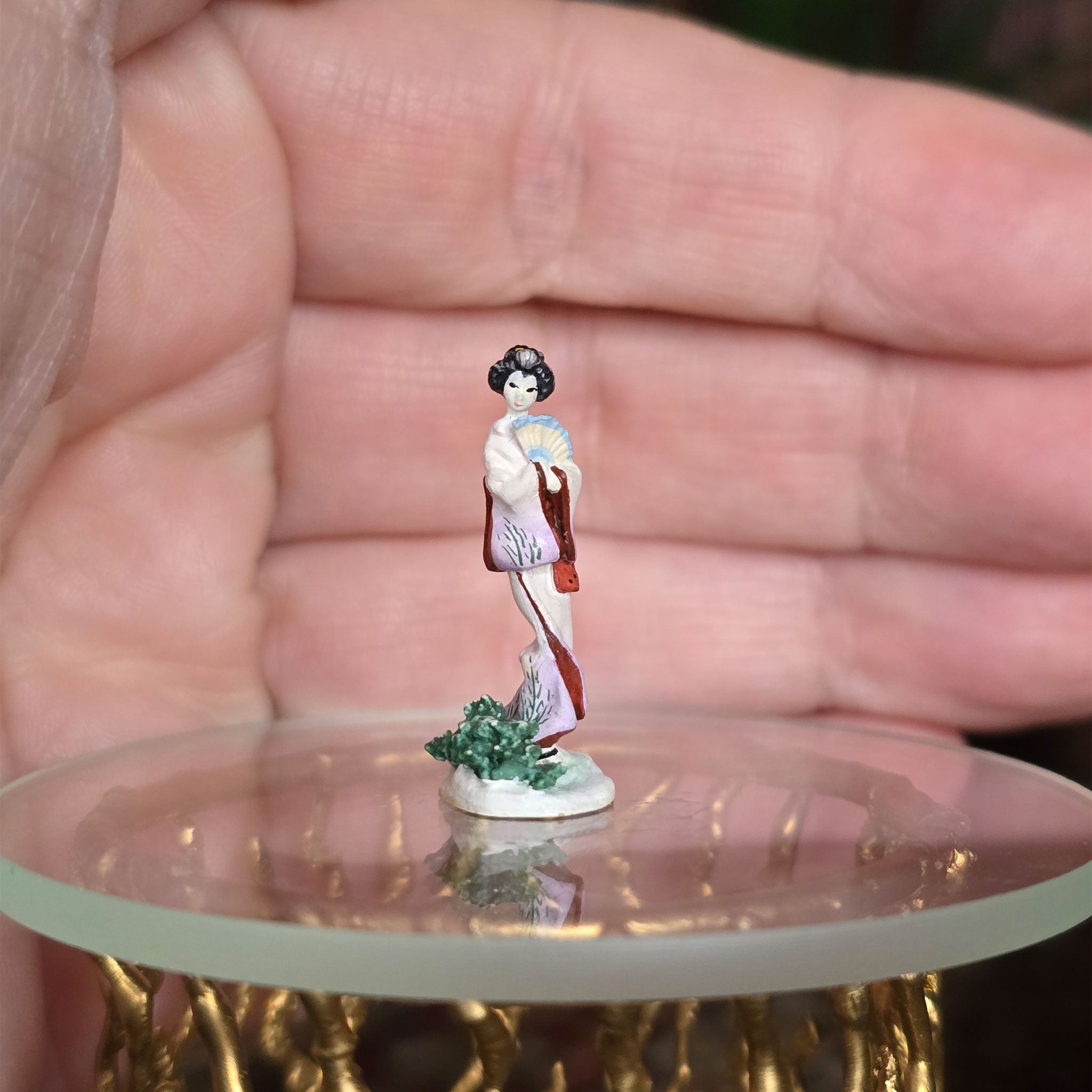 Small figurine of a woman in traditional attire on a round surface held in a hand.