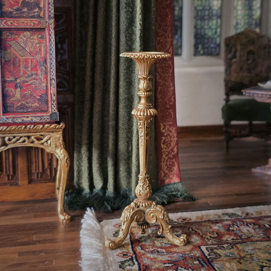 Decorative gold candlestand in an ornate room with a rug and curtains.