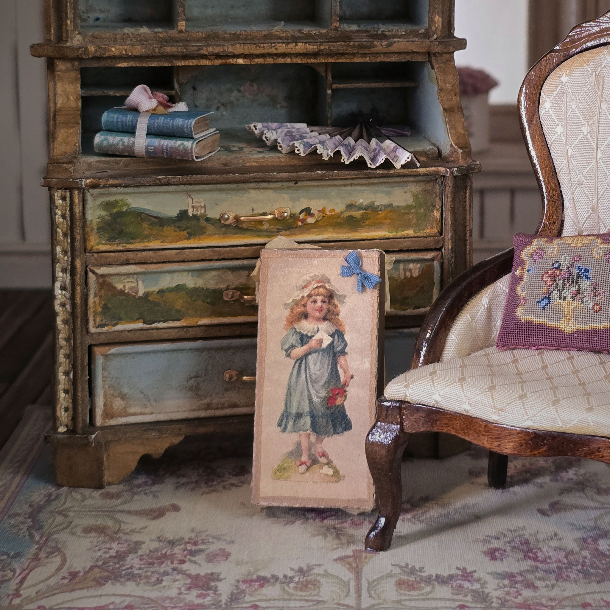 Vintage wooden desk with miniature books and a chair with a embroidered cushion on a patterned rug.