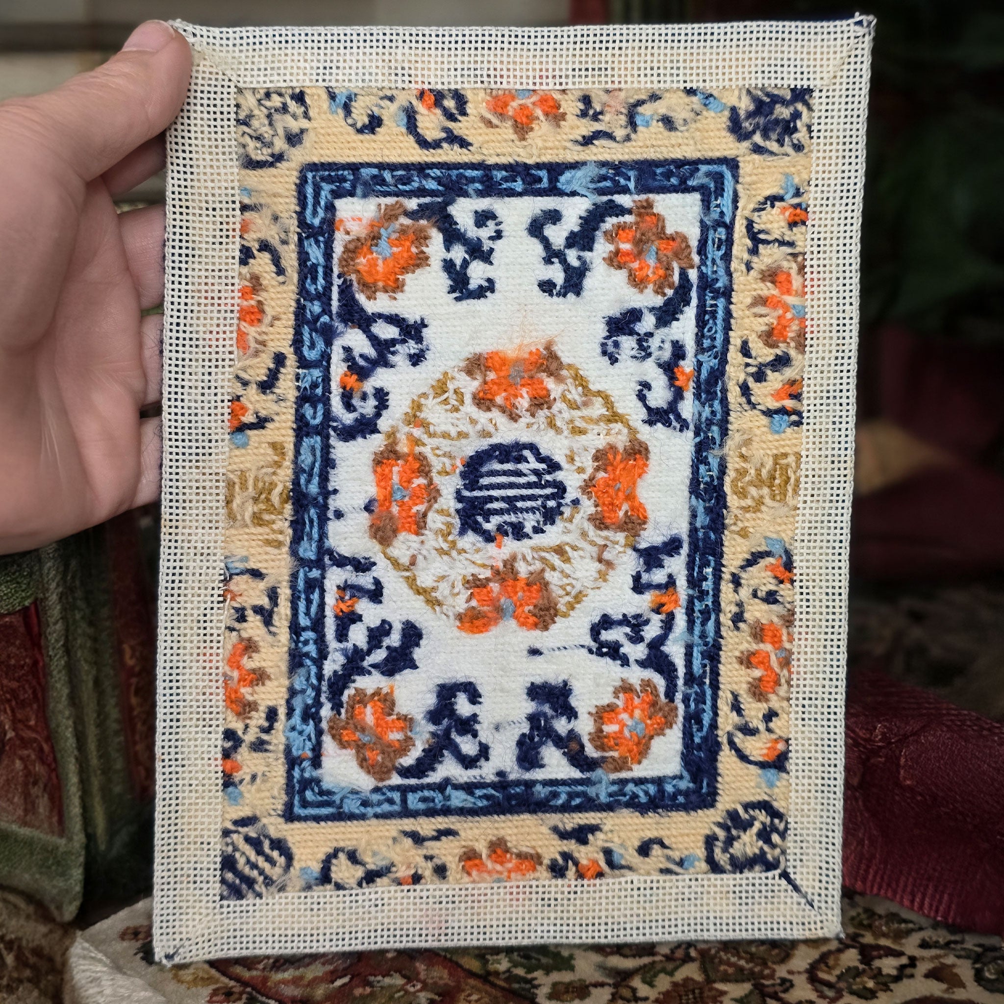 Hand holding a cross-stitched miniature rug with intricate patterns